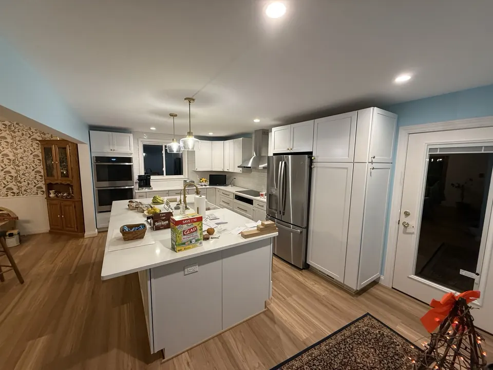 Finished kitchen remodel with white shaker cabinets, a large white island, pendant lights and stainless appliances
